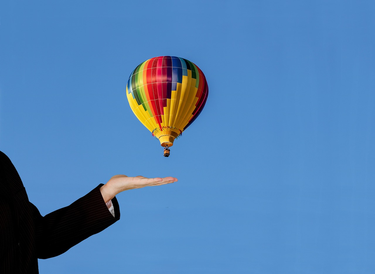 Hand held out beneath a colourful hot air balloon against a clear blue sky, a symbol of launching a brand